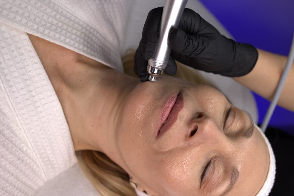 Woman in a robe receiving a facial with a handheld device
