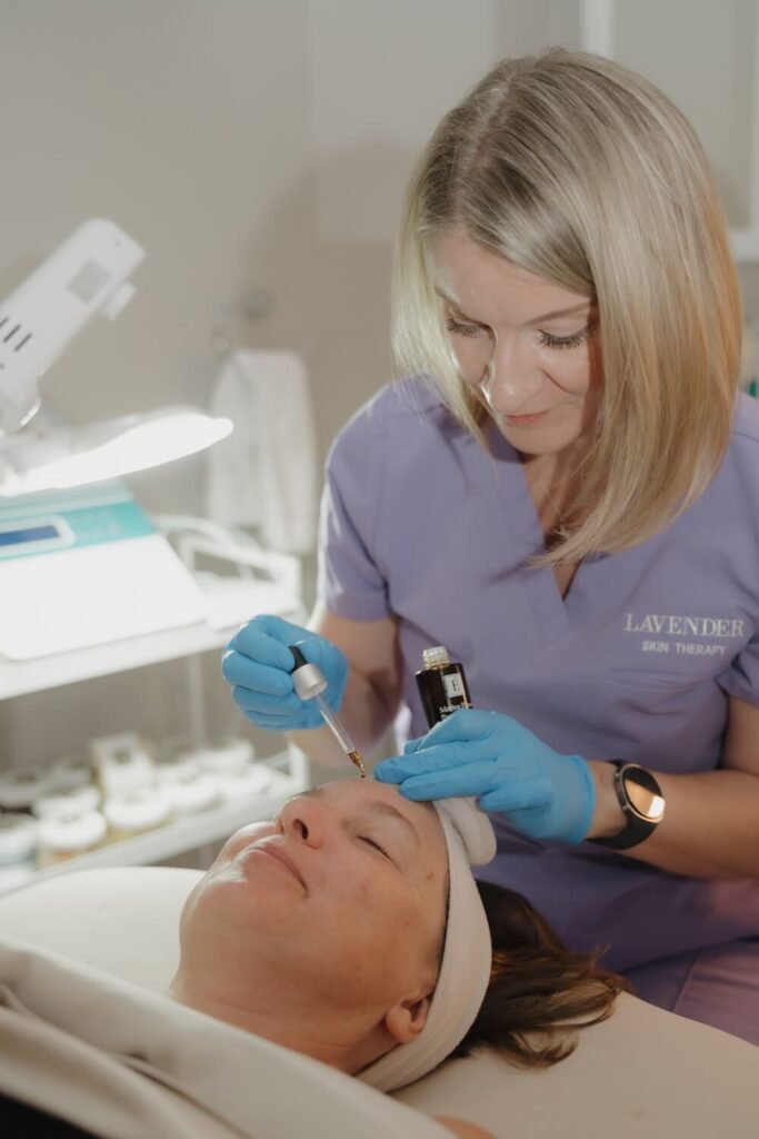 Esthetician in lavender scrubs treating a client's face with a handheld device